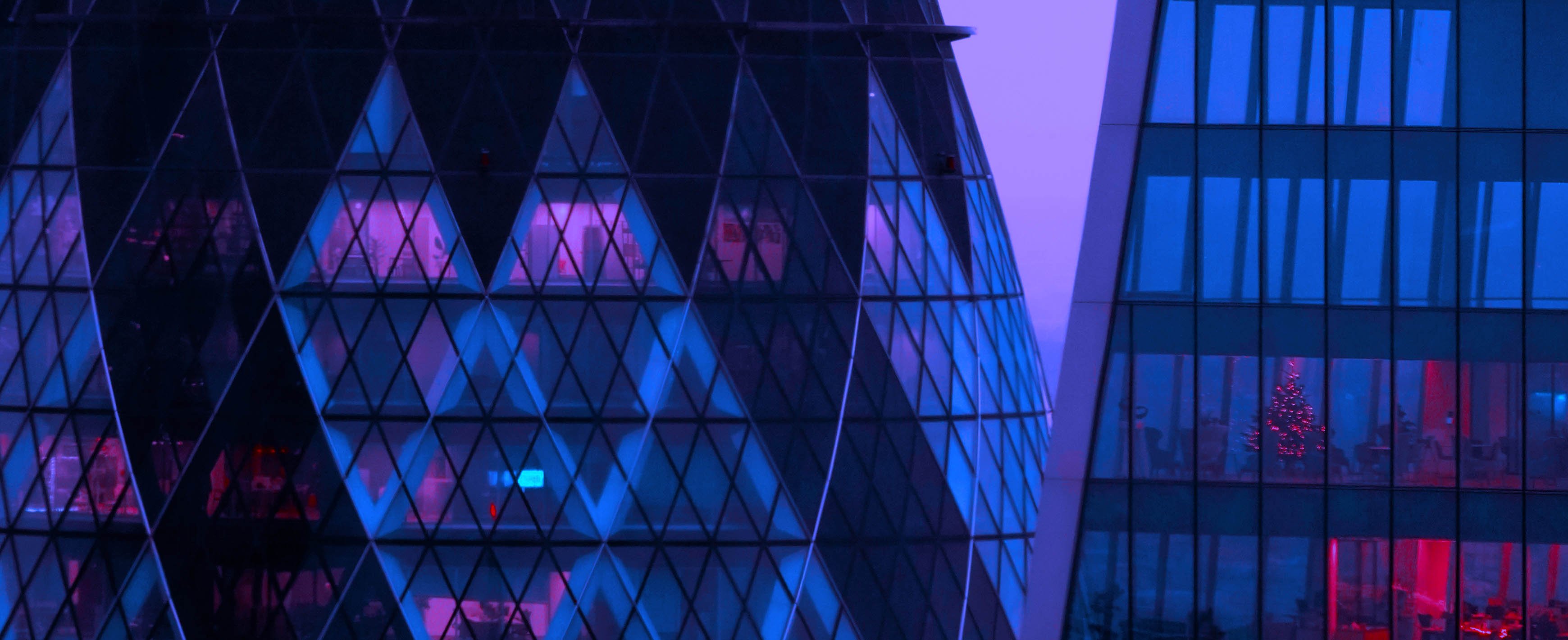 Lewis Silkin Close up of the exterior of The Gherkin building in London at dusk, the building interior is lit with hues of blue, purple and red