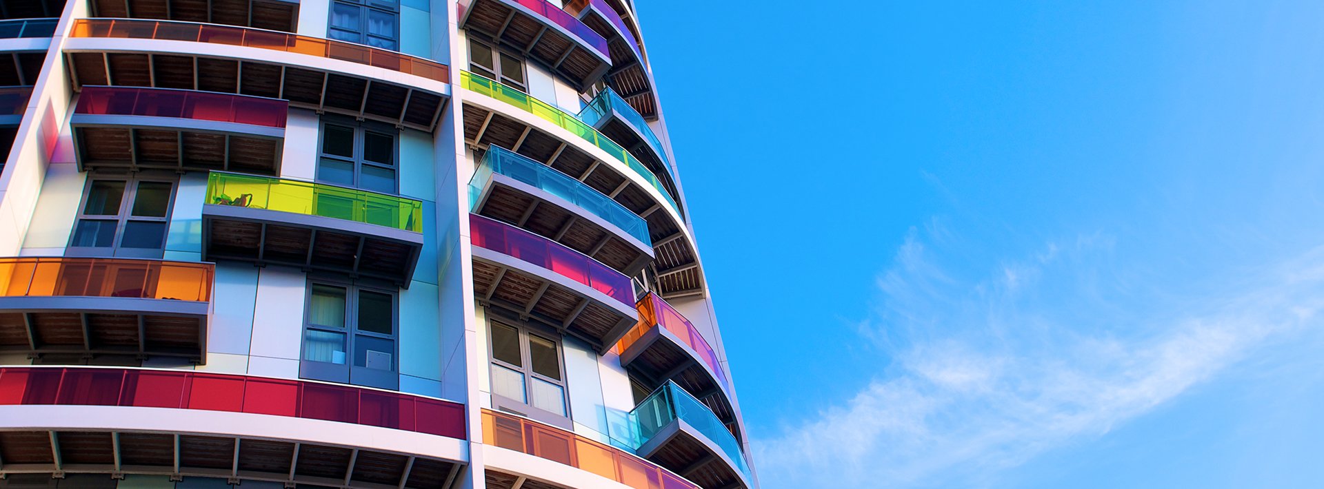 Lewis Silkin Exterior of an apartment building, each balcony has brightly coloured glass panes of pink, yellow & orange, with a blue sky