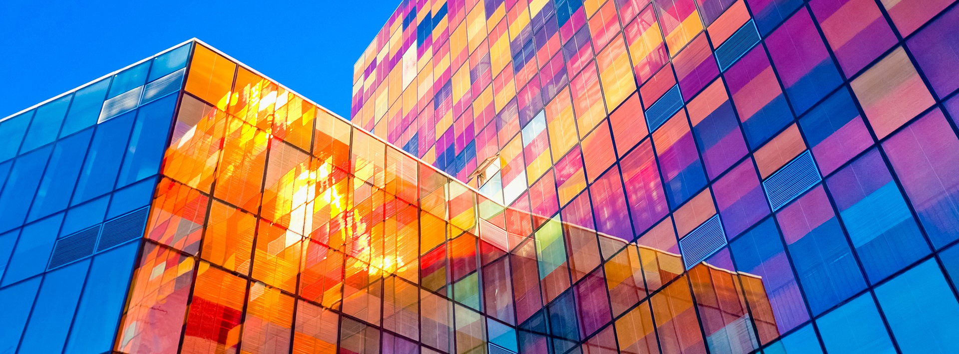 Lewis Silkin Exterior of a glass clad building with panes in a variety of autumnal shades and blues, behind is a clear blue sky