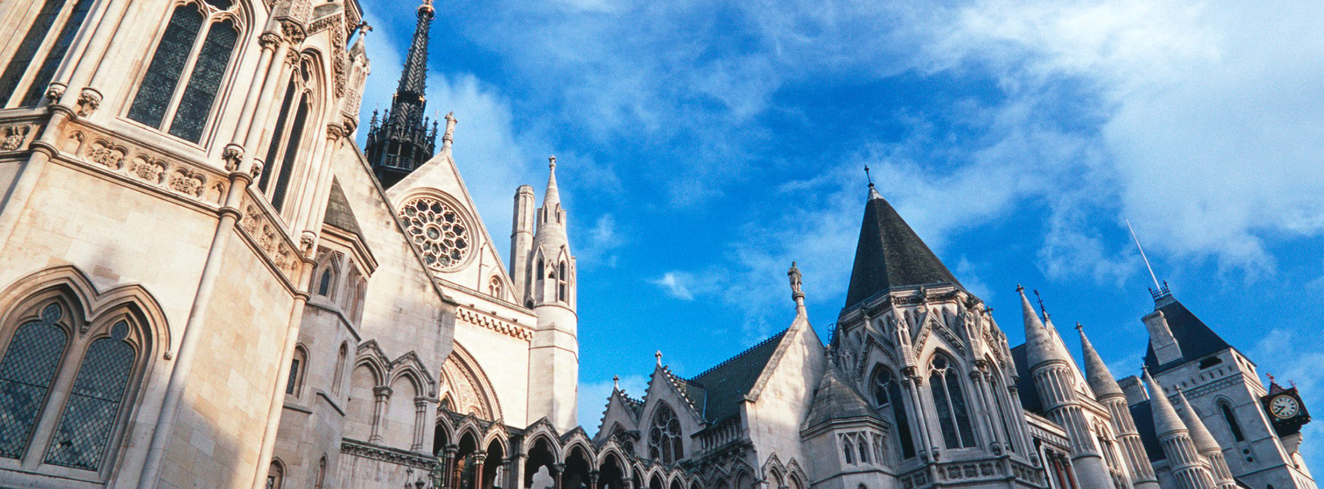 Lewis Silkin Exterior of the Royal Courts of Justice, a stunning gothic building, behind is a bright blue sky with wispy white clouds