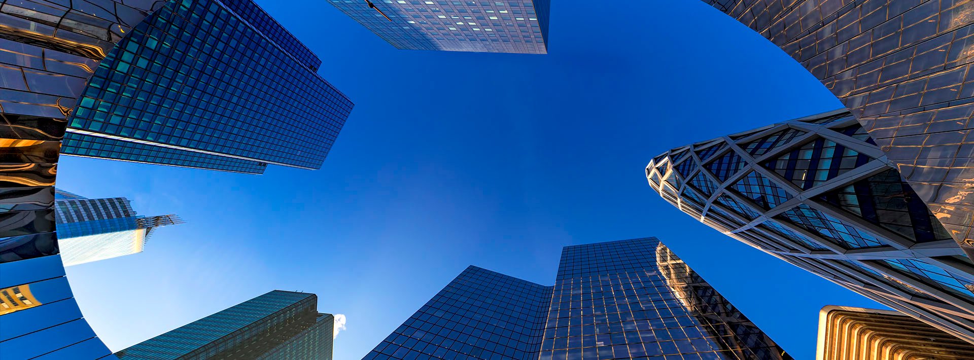 Lewis Silkin Ground level view of soaring glass office towers & blue sky seen through a teardrop shaped structure of reflective metal tile