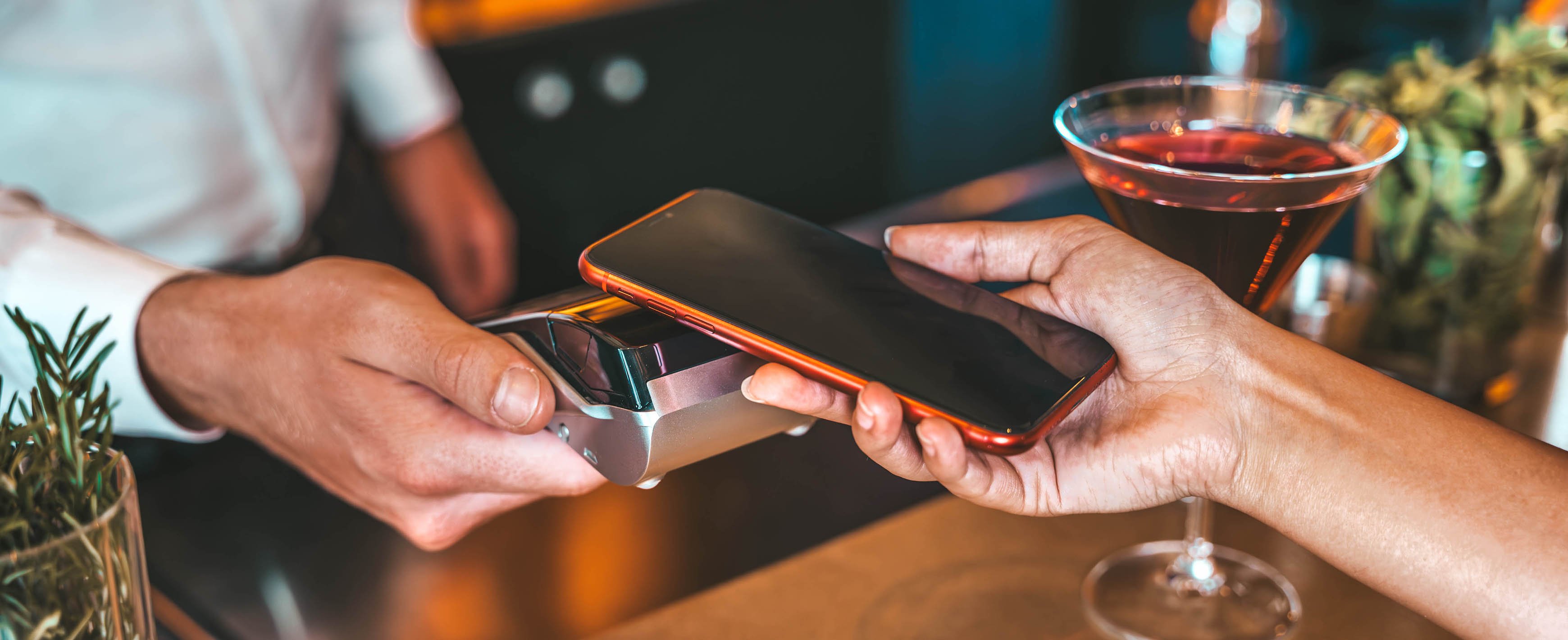 Lewis Silkin Person at a bar holding a phone to make a digital payment