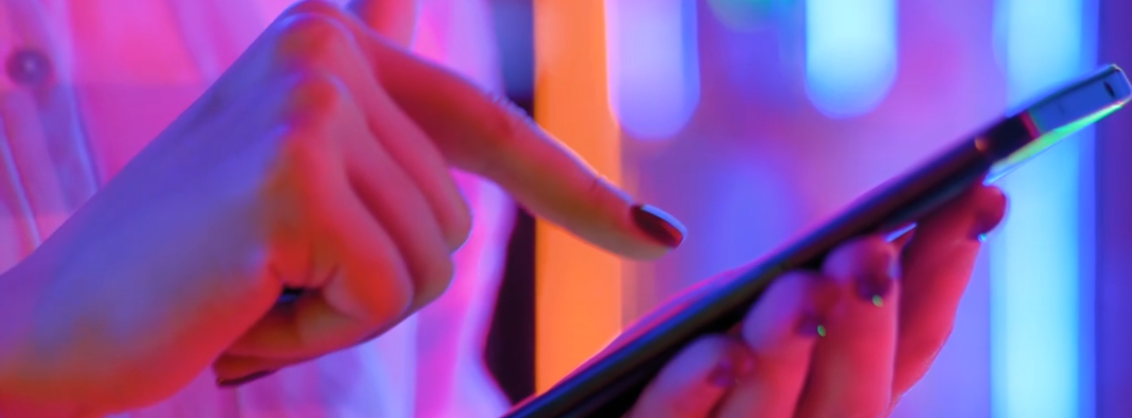 Hands using a smartphone, lit with shades of red, blue and purple
