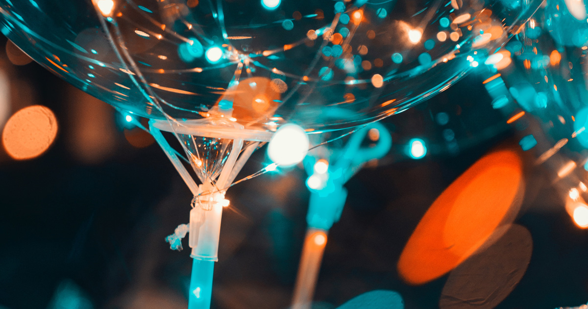 Lewis Silkin Close up of a trio of transparent party balloons reflecting hundreds of discs of blue and orange light
