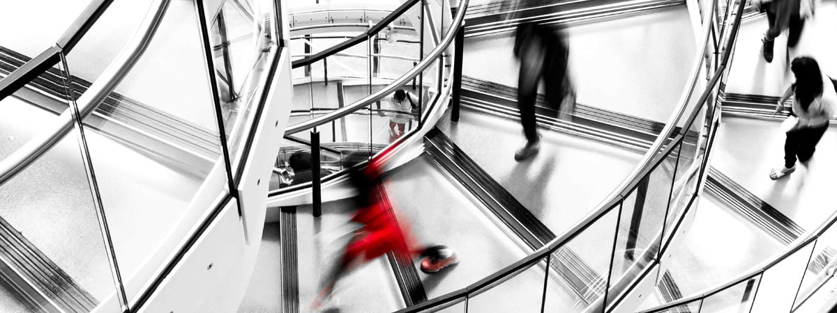 Lewis Silkin People walking a spiral staircase in black and white with the exception of one person in a red coat.