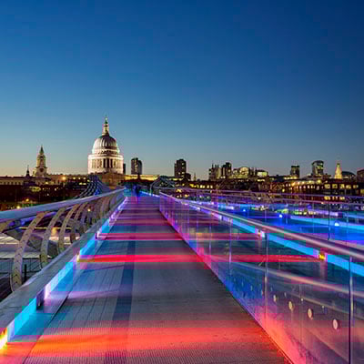 View of St.Paul's Cathedral at dusk across the Millennium Bridge which is lit in vibrant red and blue stripes