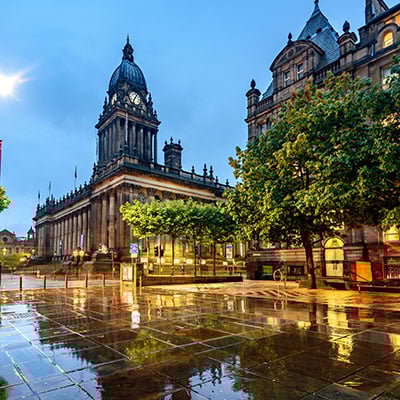 Exterior of Leeds Town Hall in the evening, wet stone floor slabs reflect bright lights and the gothic structure