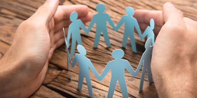 Cropped image of businessman's hands covering paper team on wooden table