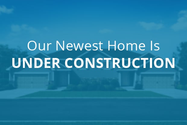 Our Newest Home is Under Construction text overlaid on out-of-focus twin home image