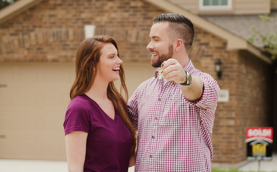 couple hugging behind their sold sign