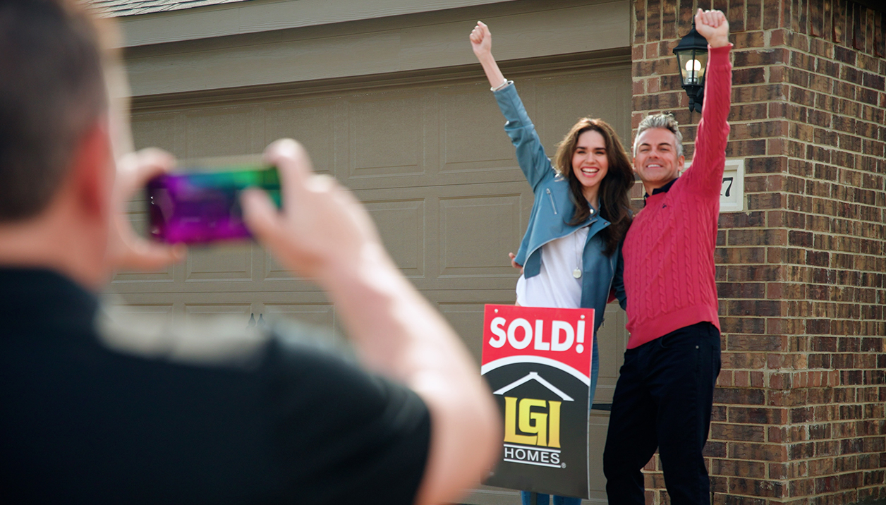 Couple with sold sign in front of home