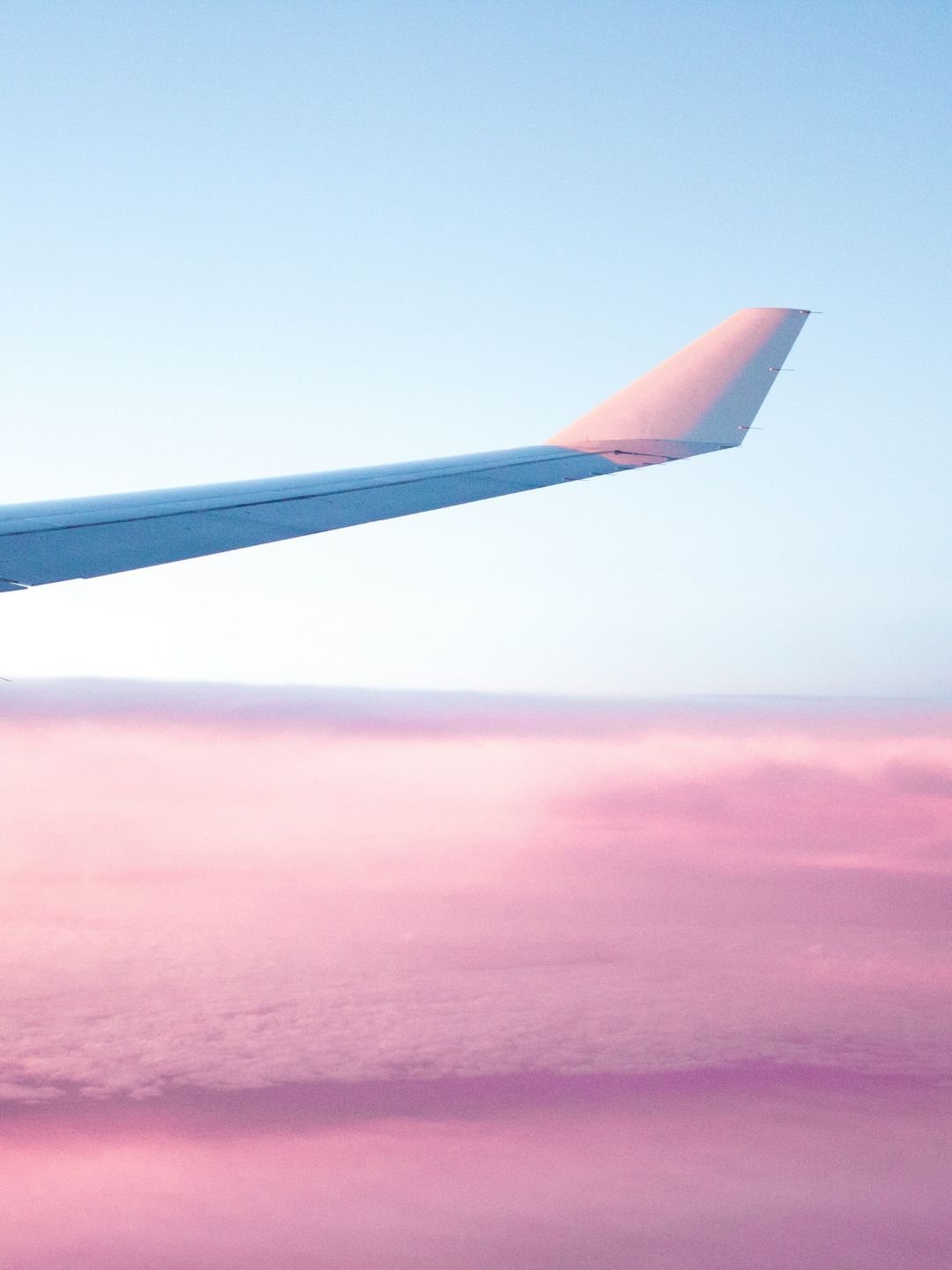wing of an airplane against pink hued clouds