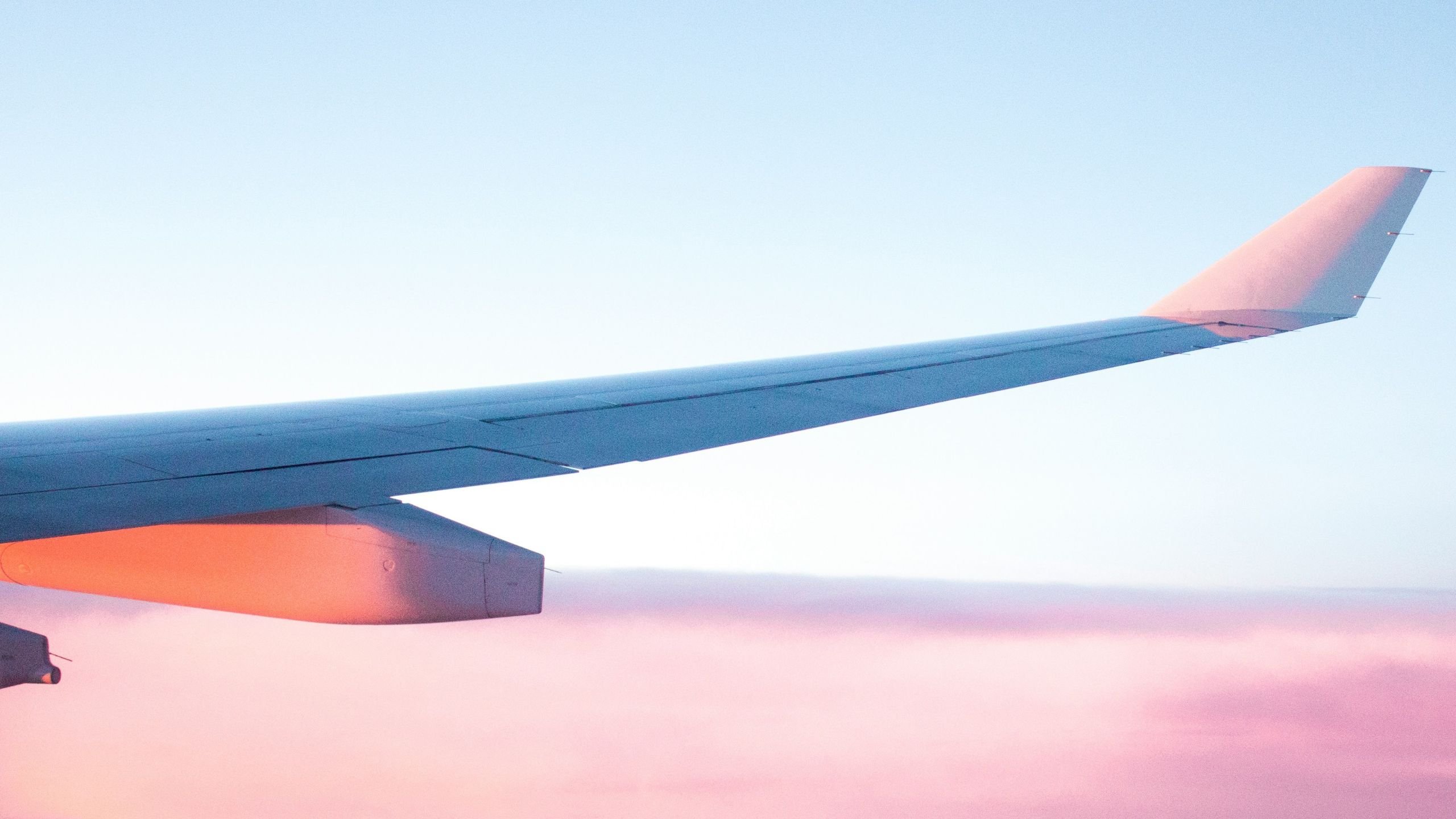 wing of a plane above pink hued clouds