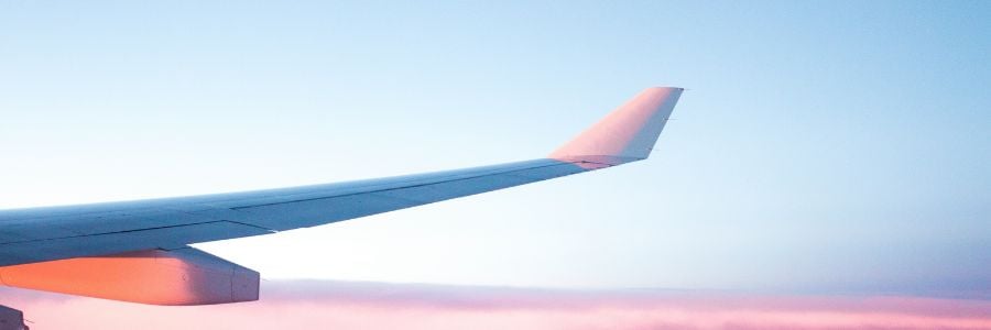 wing of an airplane about pink hued clouds