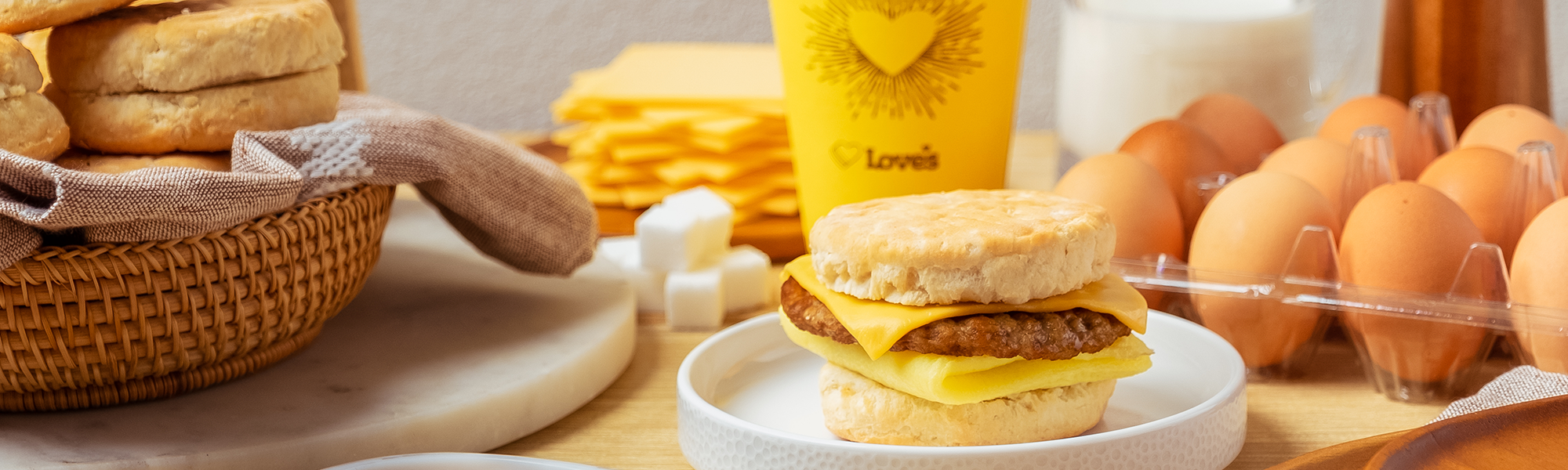 A photo of a Love's sausage, egg and cheese biscuit with eggs and biscuits in the background.