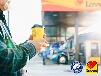 A driver holding a coffee cup in front of the diesel fueling bay with the Love's and St. Christopher Truckers Relief Fund logos