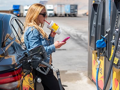 A woman fueling at a Love's while drinking a fountain drink and looking at her phone
