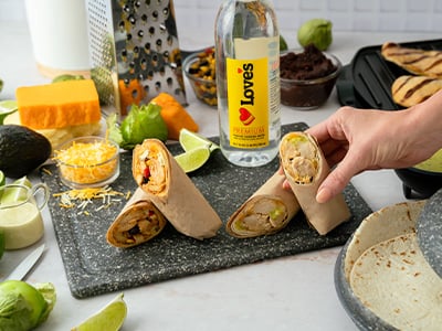 Chicken wraps on a cutting board surrounded by fresh ingredients, with a bottle of Love’s Premium purified drinking water in the background.