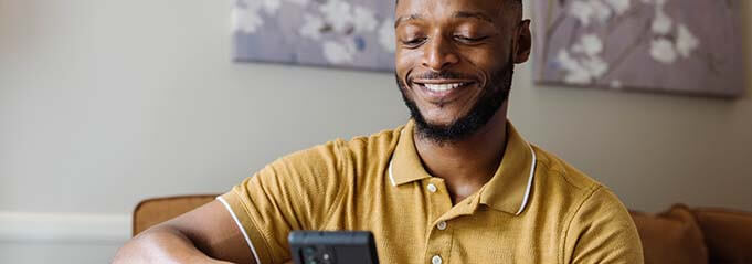 Smiling man using phone sitting at home