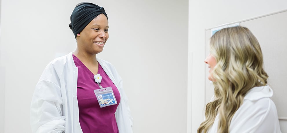 Young woman in a white top talks with a lab tech in pink scrubs and white lab coat