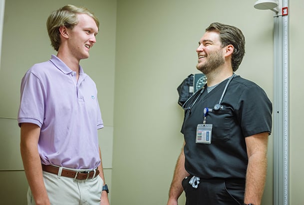Young man in a pastel shirt speaking with a health care worker in dark scrubs