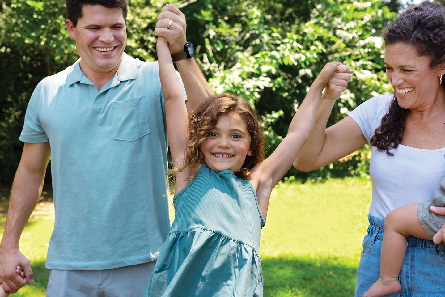 Man and woman holding baby swinging child in the middle while she smiles happily
