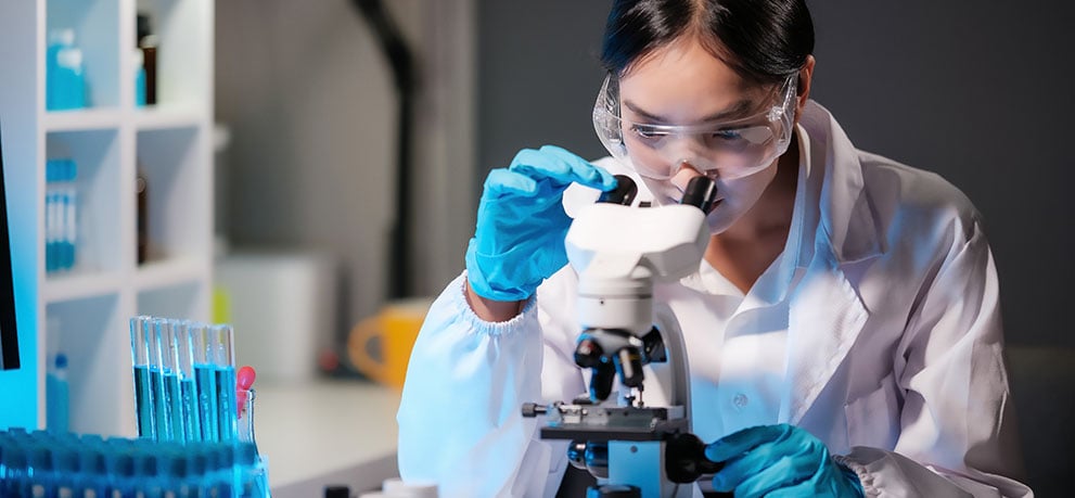 Woman in a lab coat looks into a microscope