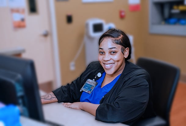 Medical professional sitting at a computer and smiling toward the camera