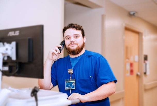 Man in blue scrubs talking on phone at a computer kiosk