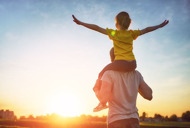 Young girl sitting on father's shoulders during a sunrise