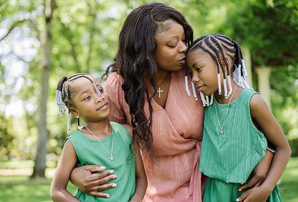 Mom kisses daughter while hugging another daughter