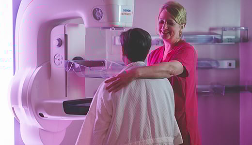 Technologist assists robe-draped woman with mammogram with kind smile