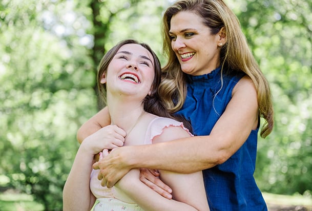 Mother and daughter smiling and hugging outside 