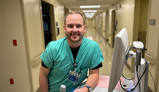 health care worker in scrubs leaning next to a computer screen