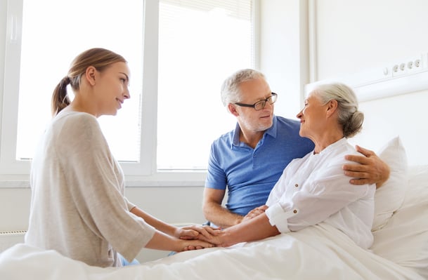 Kind woman talking to older woman in hospital bed