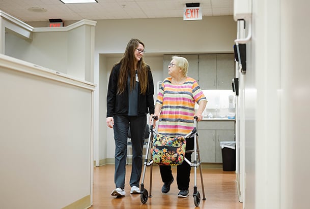 Older woman with a walker walking next to a nurse in the clinic
