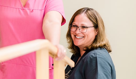 Therapist smiles while assisting patient walking between bars