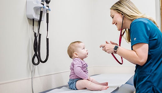 Health care provider in blue scrubs examines a baby girl 