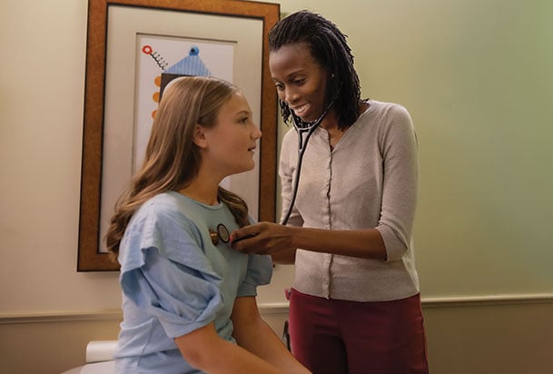 Doctor examines preteen girl in exam room