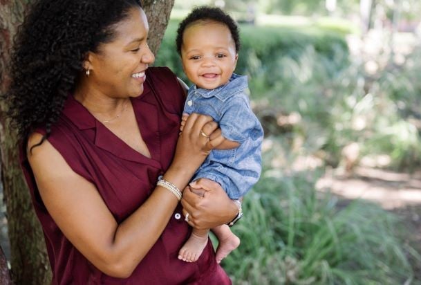 mother holding and cuddling infant son outside, both smiling