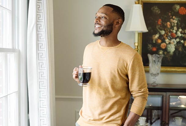 Man drinking coffee and smiling while gazing out window of a home