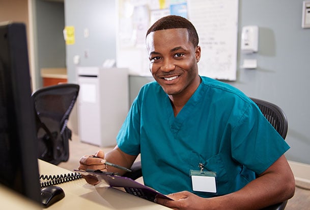 Health care provider with a clipboard sitting at a computer and smiling toward camera