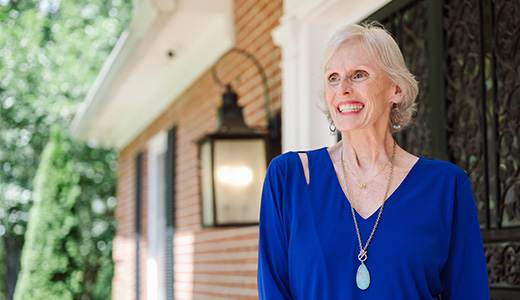 woman in a blue shirt and necklace standing in front of a house
