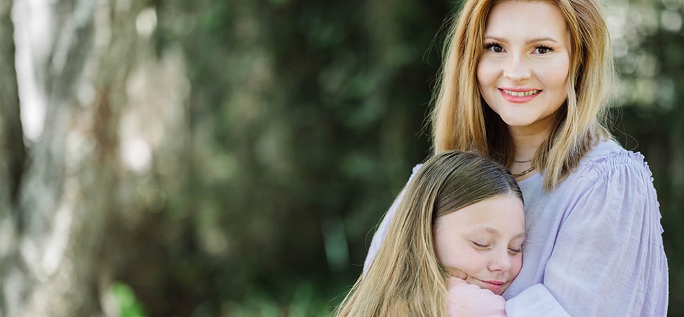 A woman looking into the camera smiling while she hugs her daughter