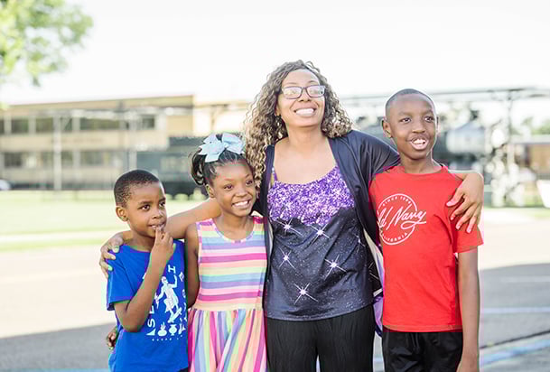 Mother standing with her arms around her younger son and daughter on the left and an older son on the right