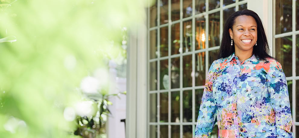 Smiling woman in a bright patterned top standing outside a set of French doors on a sunny day