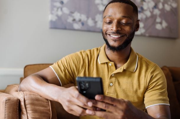 Man in mustard yellow top smiling and looking at phone in brown leather chair