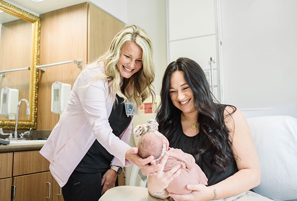 Young mother smiling at her newborn as a nurse leans over and supports baby's head