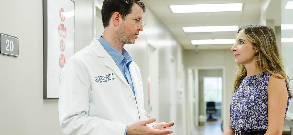 Doctor in a lab coat explaining something to a woman in a blue flowered dress