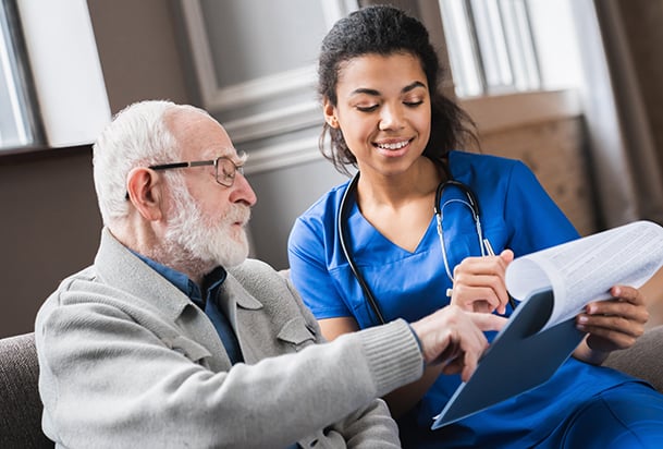 An older man and a woman in blue scrubs looking at a clipboard together